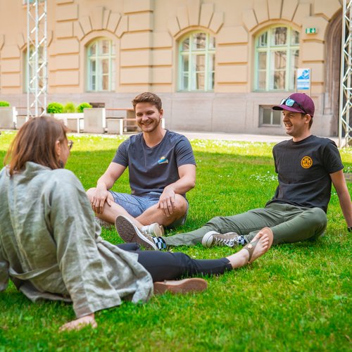 Studierende sitzen auf dem Gras und amüsieren sich.